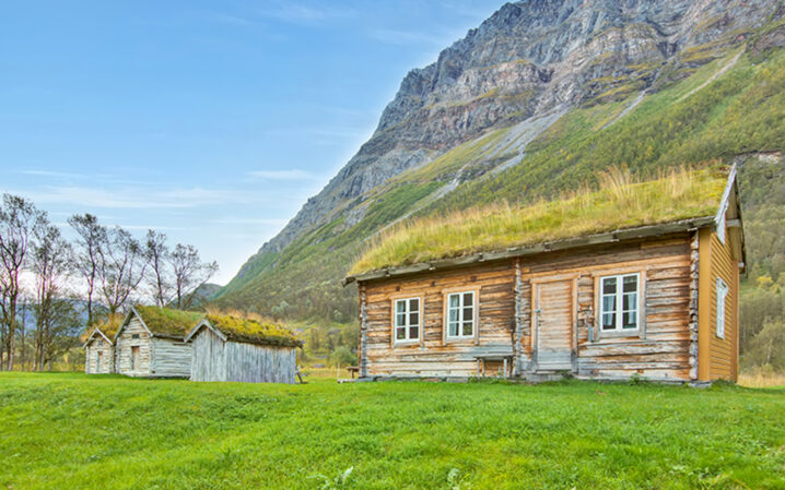 Ett stort og tre små gamle hus på en gresslette med et fjell i bakgrunnen