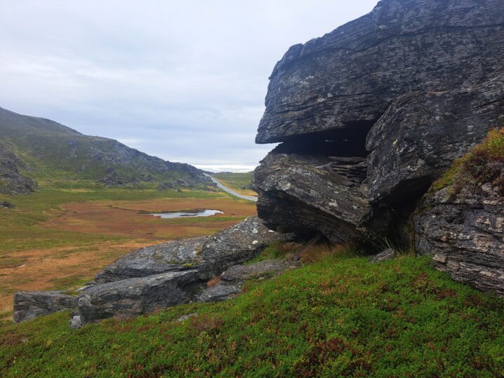 Stor klippe til høyre i bildet. Til venstre en stor slette i høstfarger og en vei lengst borte.