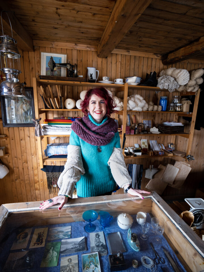 Kvinne i museumsbutikk. Disk i glass foran og hyller med mange gamle gjenstander bak.