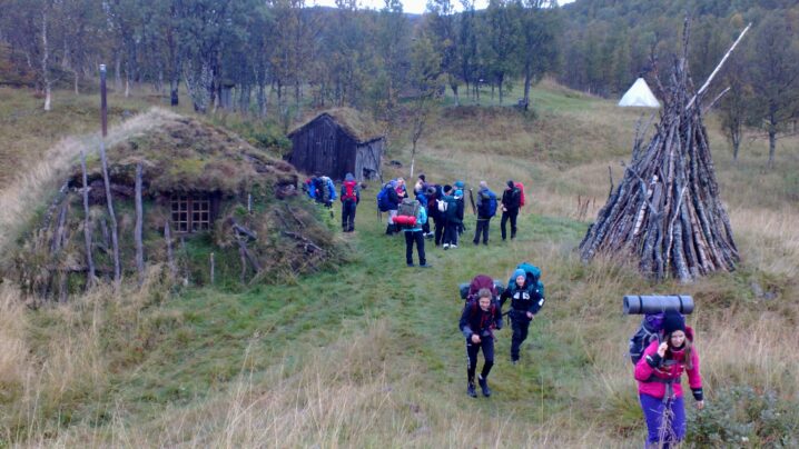 Lavvo, gamme og hus på Vilegesvárre med flere besøkende som bærer sekk