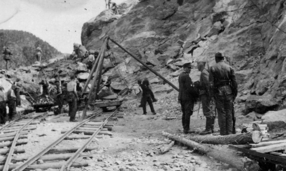 Svart hvitt bilde. Viser soldater og krigsfanger. Krigsfanger jobber med å lage vei.