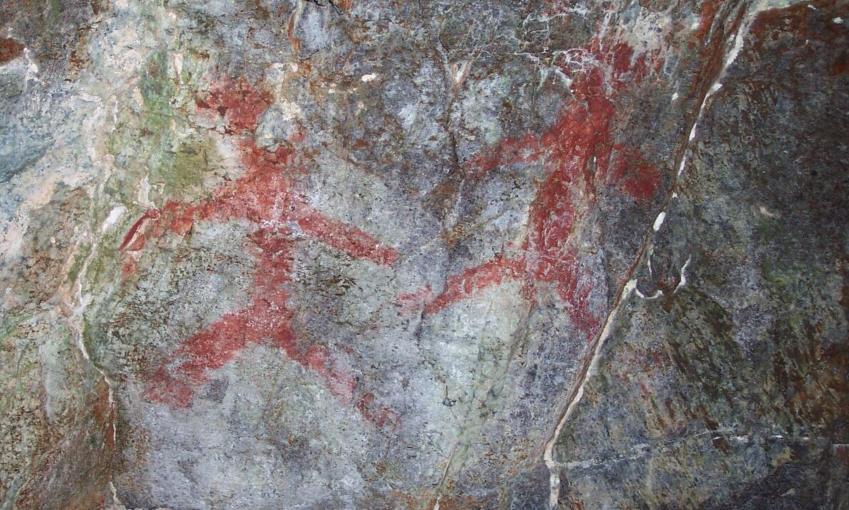 Hulemalerier av to mennesker tegnet i rødt på grått berg.