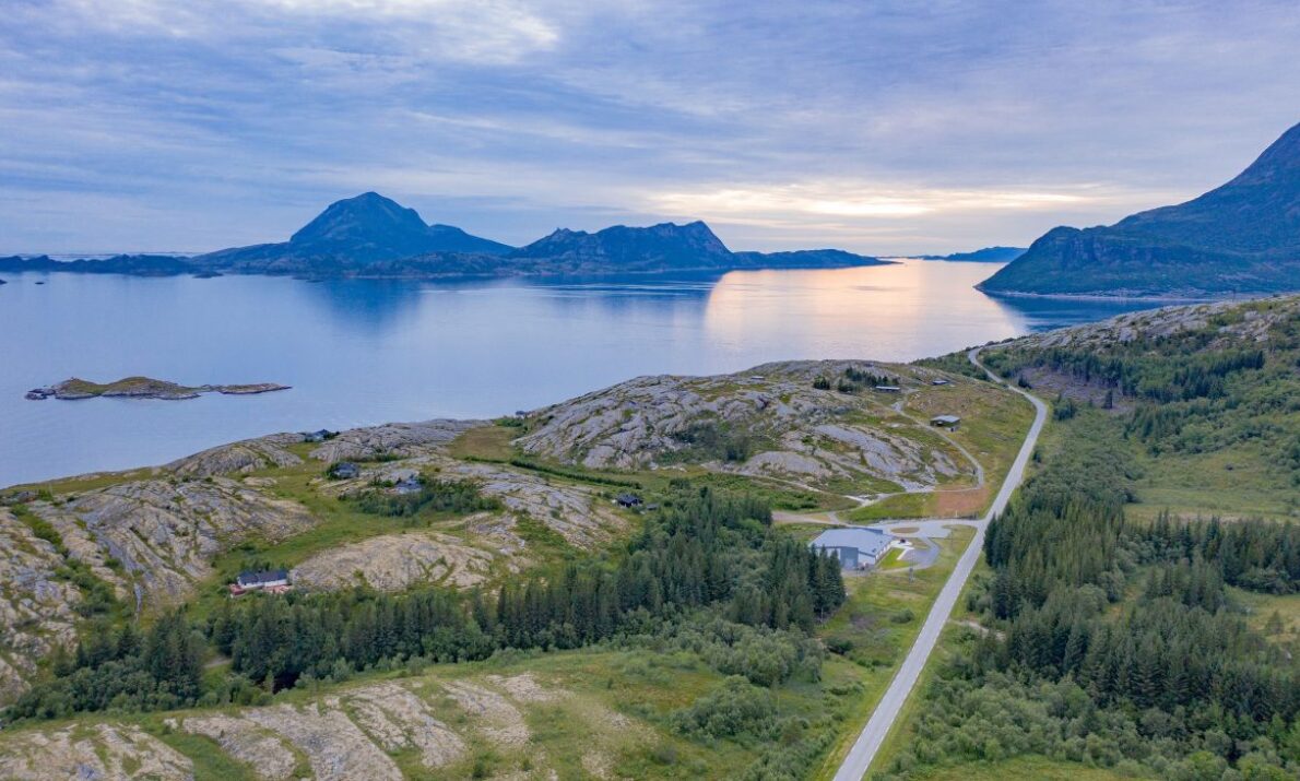 Kystfort ligger i landskapet omringet av gressenger og berg. En vei krysser landskapet. I bakgrunnen havet, noen lave fjell og en himmel med tett skydekke.