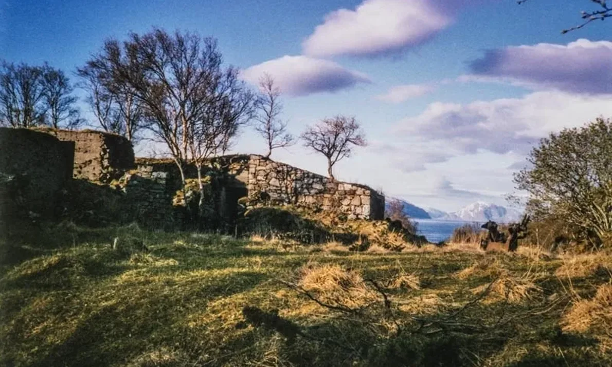 Ruin av et fort midt i bildet. Vegetasjon rundt. Noen trær rundt. Blå himmel med noen skyer.