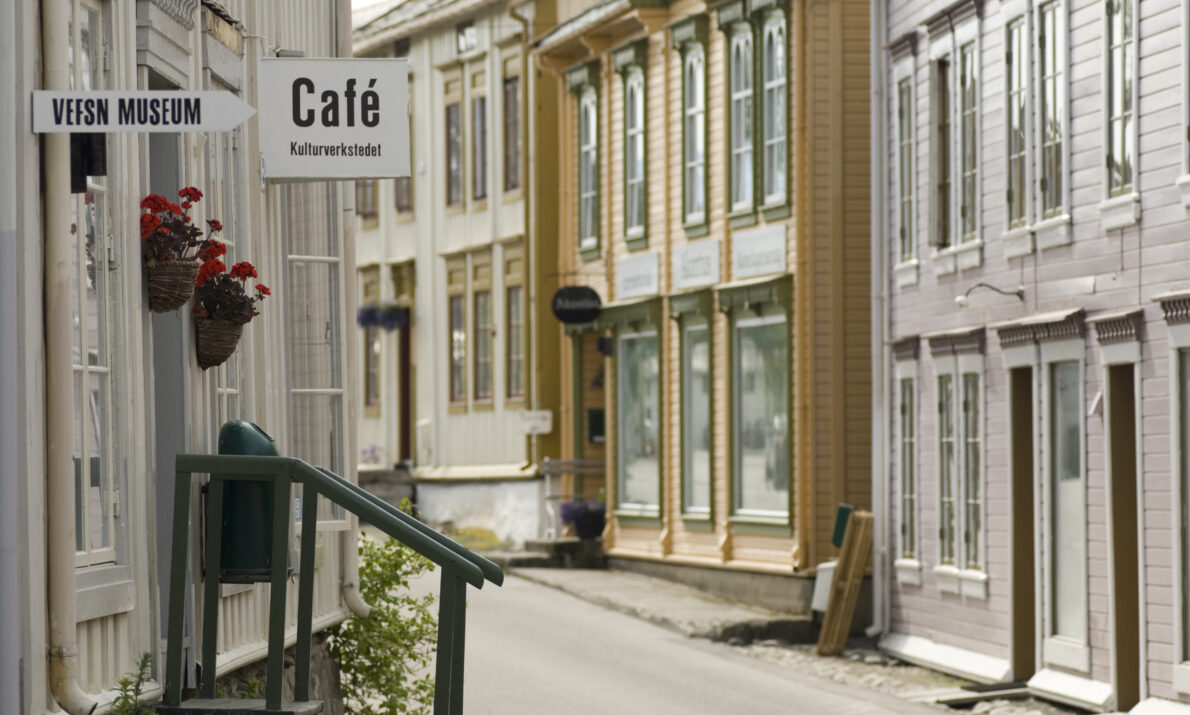 "En sjarmerende gate med gamle trehus i skandinavisk stil, med skilt for et museum og en kafé."