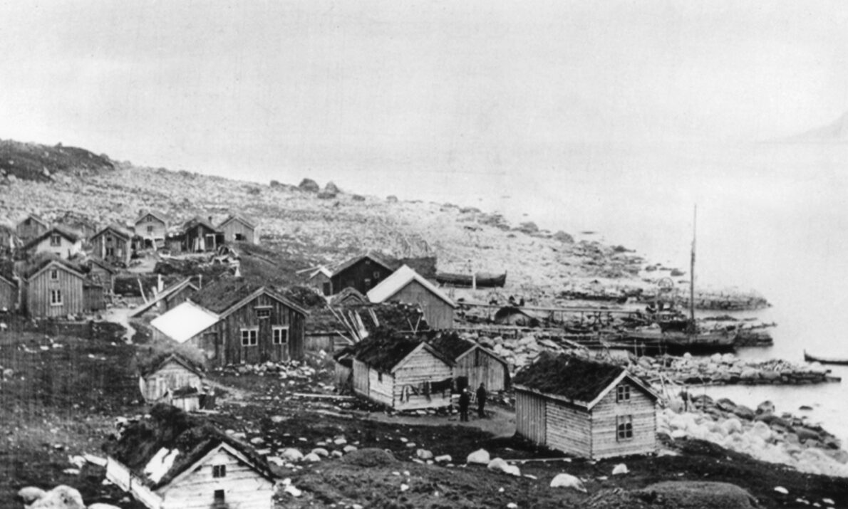 Svart hvitt bilde. Fiskevær ved fjorden.