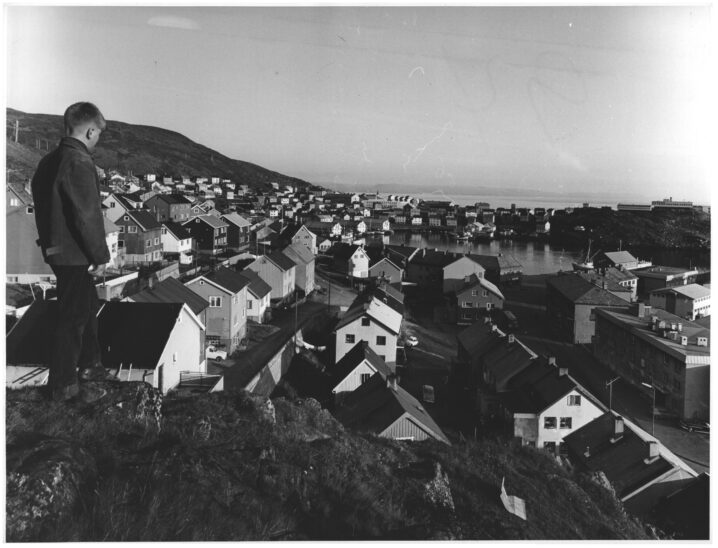 Svart hvitt bilde. Ung mann står og ser utover Honningsvåg sentrum.