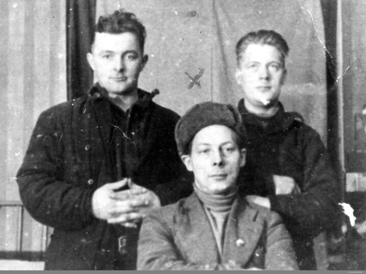 Svart hvitt bilde. To menn stor og en sitter foran. Gardin eller lignende bak.