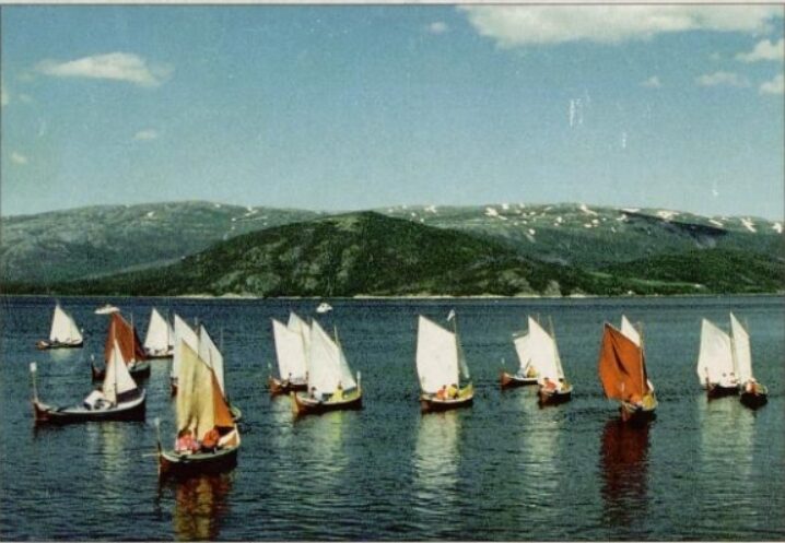 Regatta med Bindalsbåter. Ligger på vannet med seil. Åser og fjell i bakgrunnen.