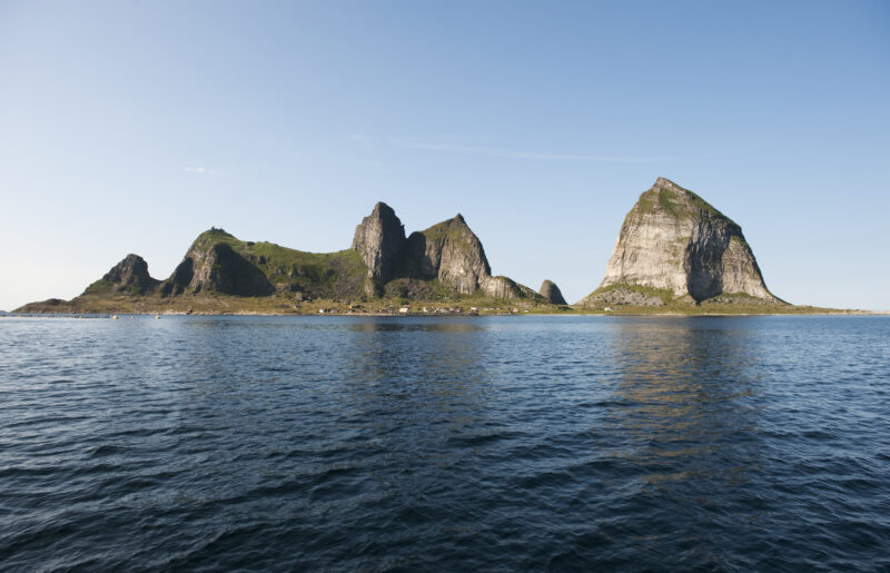 Øygruppe med kvasse fjell stikker opp av havet. Blå himmel over.