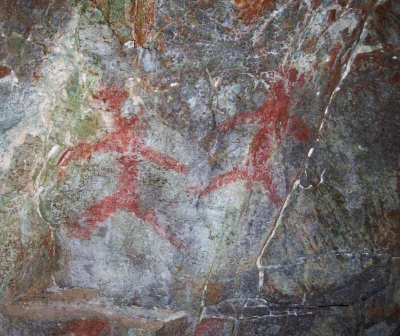 Hulemalerier av to mennesker tegnet i rødt på grått berg.