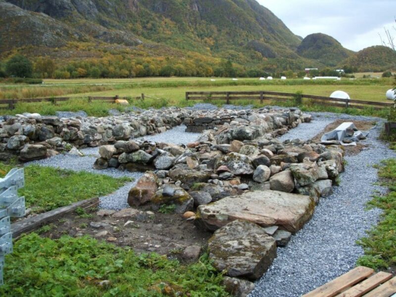 Ruiner av en kirke i forgrunnen. Grønn eng lenger bak og et grønnkledt fjell i bakgrunnen. Himmel med skyer lengst bak.