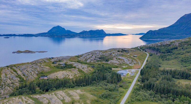 Kystfort ligger i landskapet omringet av gressenger og berg. En vei krysser landskapet. I bakgrunnen havet, noen lave fjell og en himmel med tett skydekke.