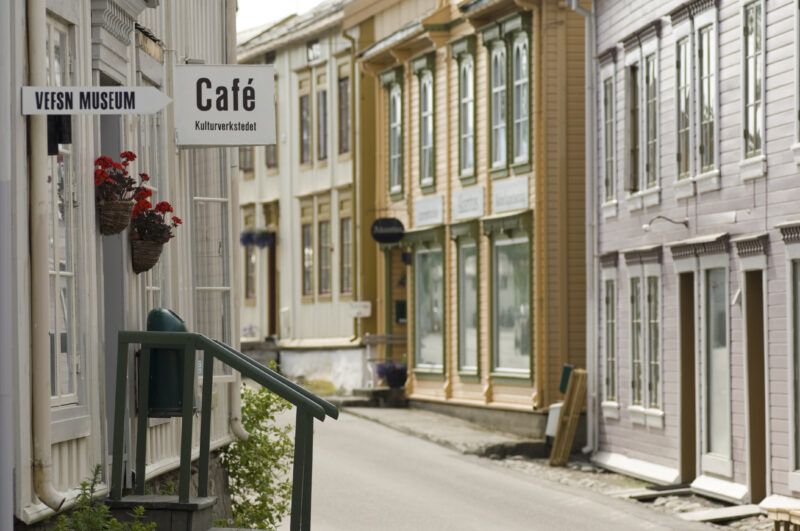 "En sjarmerende gate med gamle trehus i skandinavisk stil, med skilt for et museum og en kafé."