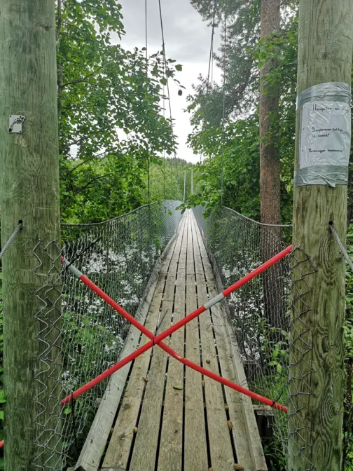 Hengebru i skogkledt landskap med røde tau i kryss foran.